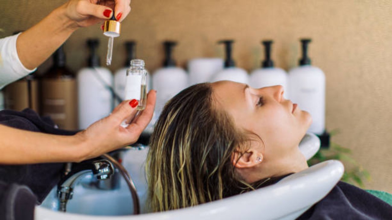 Beautiful young woman getting her hair washed in hair salon. She is relaxing with her eyes closed while the hairdresser massages her scalp and washes her hair with shampoo, hair treatment and water.