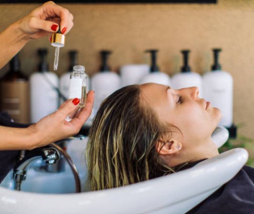 Beautiful young woman getting her hair washed in hair salon. She is relaxing with her eyes closed while the hairdresser massages her scalp and washes her hair with shampoo, hair treatment and water.